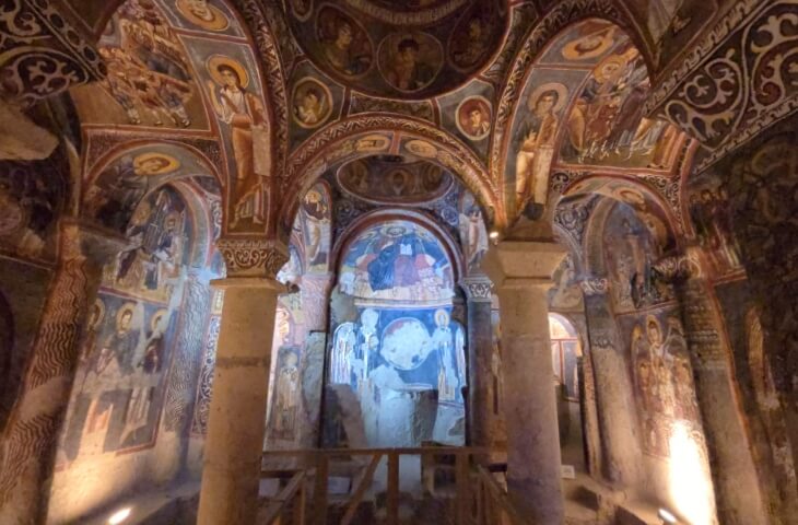 Karanlık Kilise’nin iç mekanı, tavan ve duvarları tamamen İncil temalı fresklerle kaplı. Orta bölümde sütunlar, kemerler ve aziz tasvirleri görülüyor.